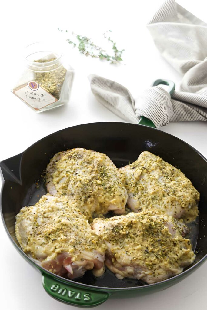 Four raw, herb-seasoned chicken thighs in a black skillet on white surface.