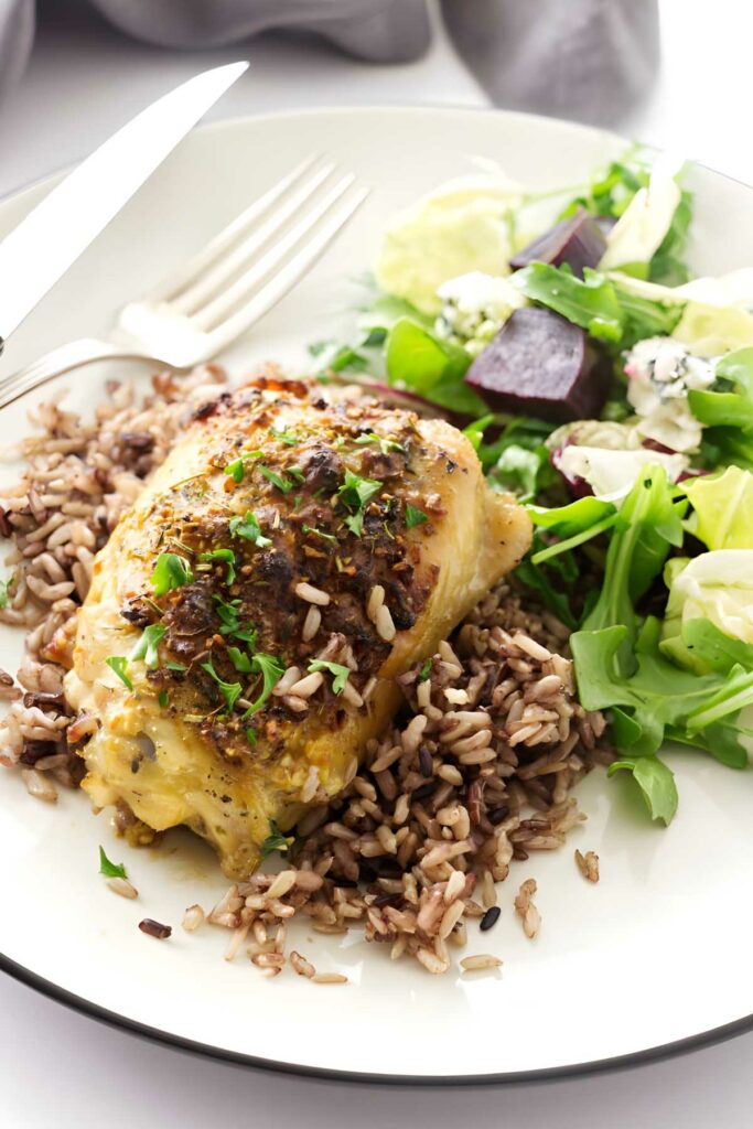 Baked chicken breast on wild rice with green salad and utensils on plate.