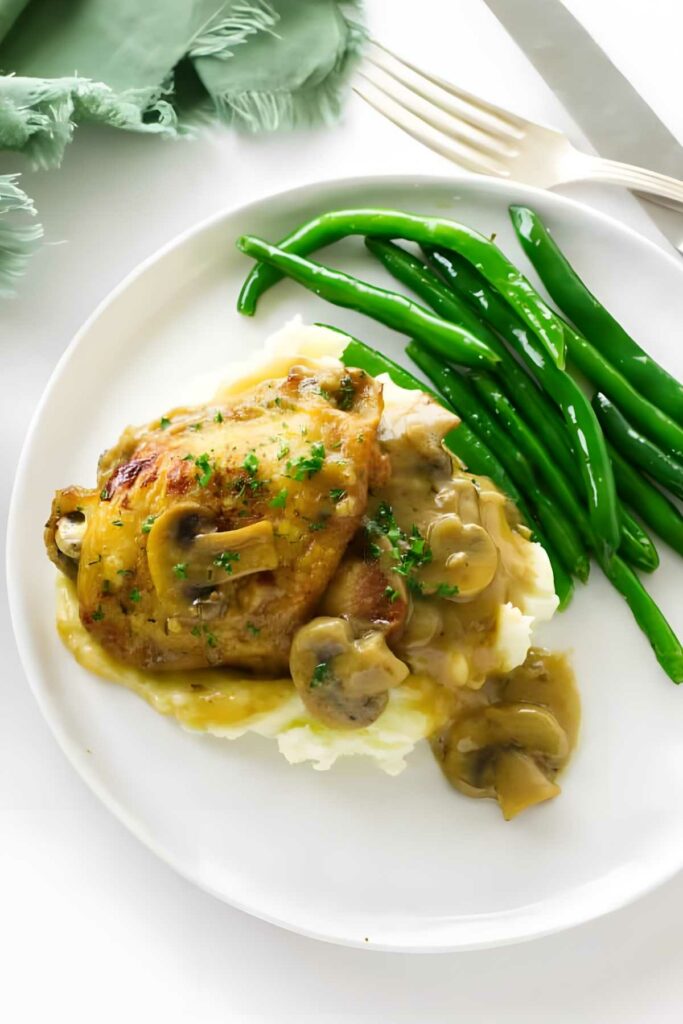 Plate of chicken, mashed potatoes with gravy, herbs, and green beans.