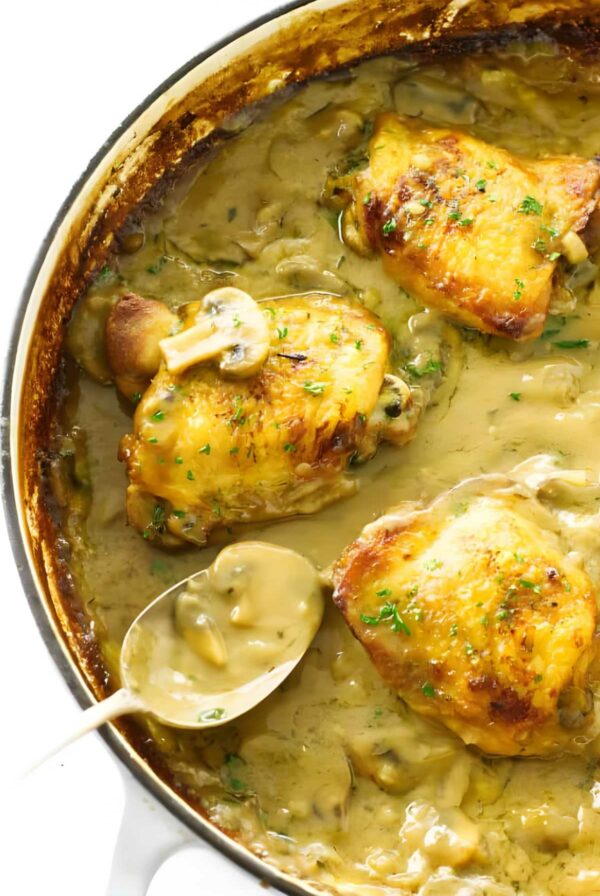 Chicken thighs in creamy mushroom sauce, skillet, garnished with herbs.