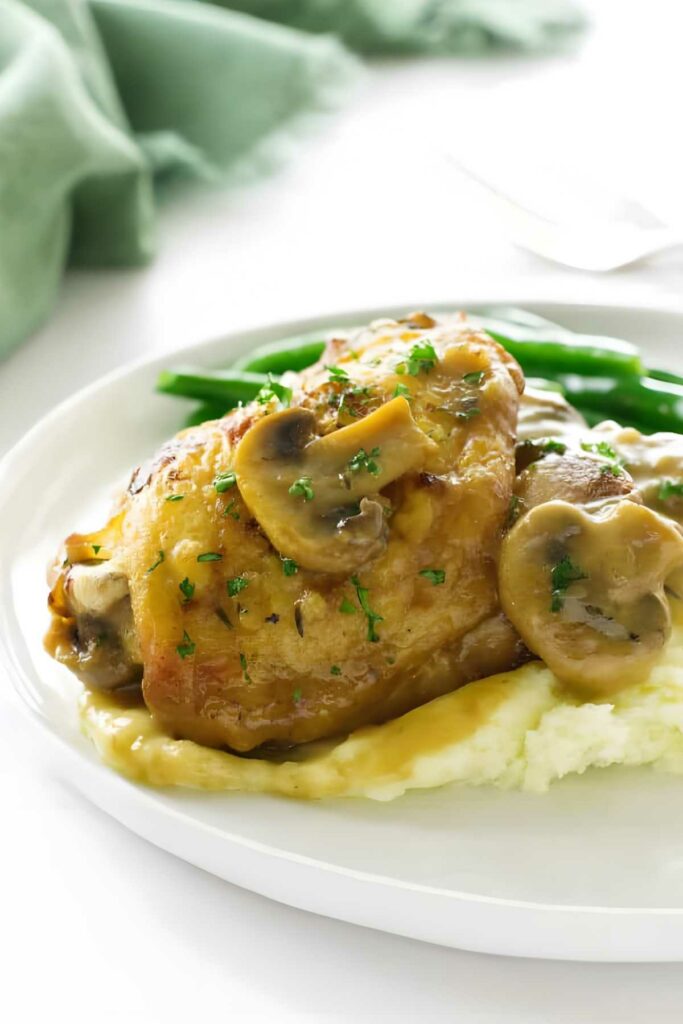 Chicken with mushrooms in sauce over mashed potatoes, green beans in background.