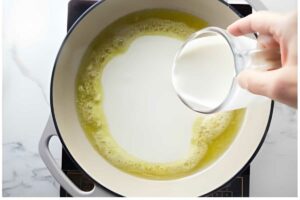 Hand pours milk into melted butter in a skillet.