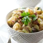 Creamy pasta salad with parsley in a white bowl, vintage fork beside.