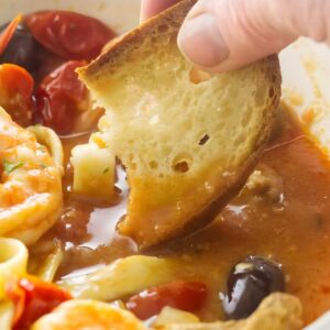 Hand dips crusty bread into shrimp, pasta, and tomato.