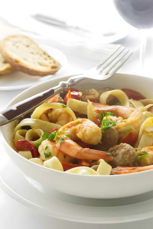 Bowl of pasta with shrimp, chorizo, tomatoes, herbs, and parsley garnish.