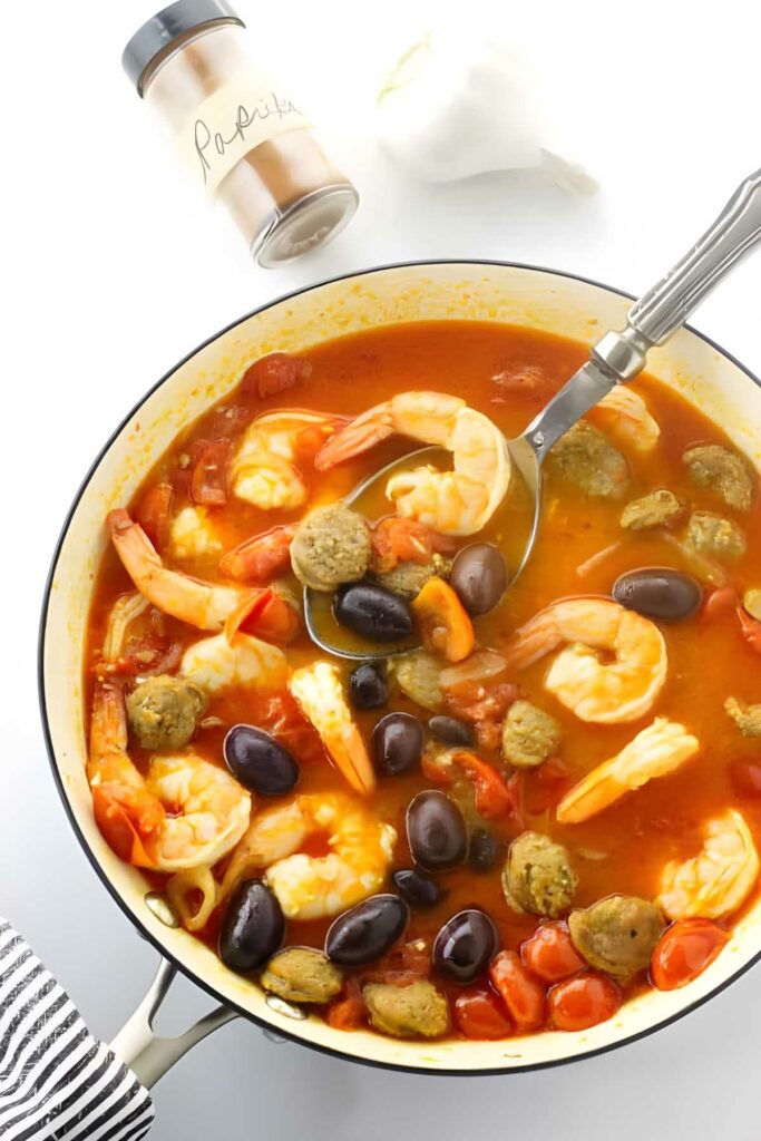 Pot of shrimp pasta with sausage, olives, and shrimp; spoon inside.