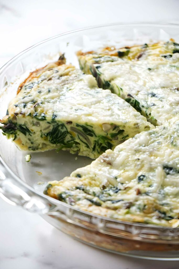 Spinach and cheese quiche in a glass dish, one slice removed.