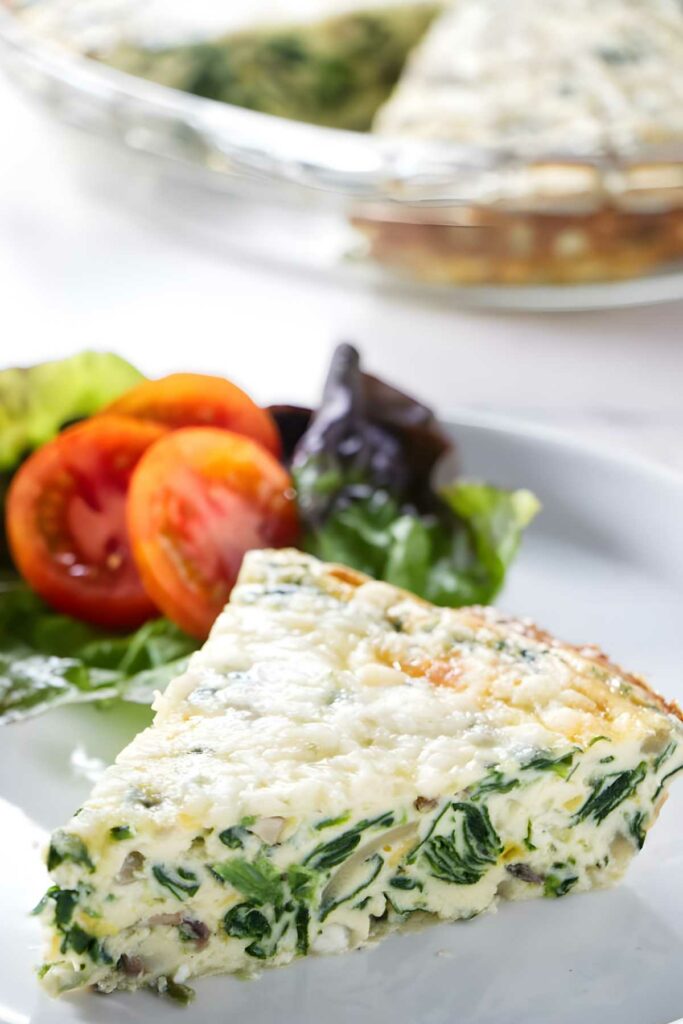 Slice of spinach and cheese quiche with side salad on a white plate.