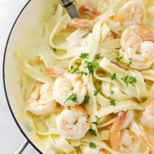 Fettuccine with shrimp in creamy white sauce, topped with parsley in skillet.