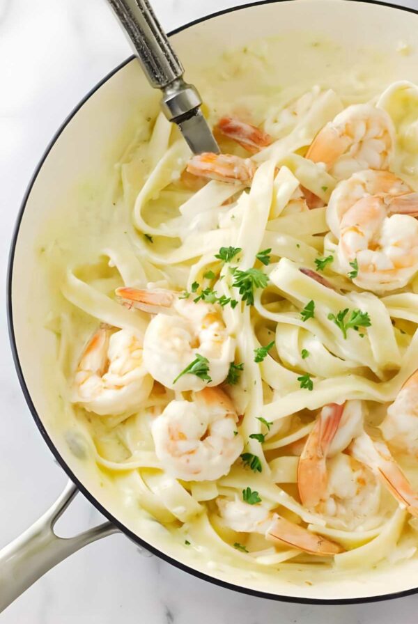 Fettuccine with shrimp in creamy white sauce, topped with parsley in skillet.