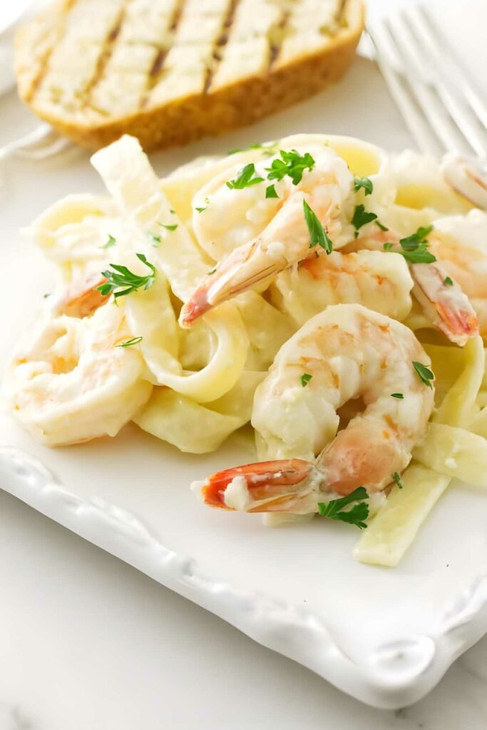 Shrimp fettuccine Alfredo with parsley and grilled bread on a plate.
