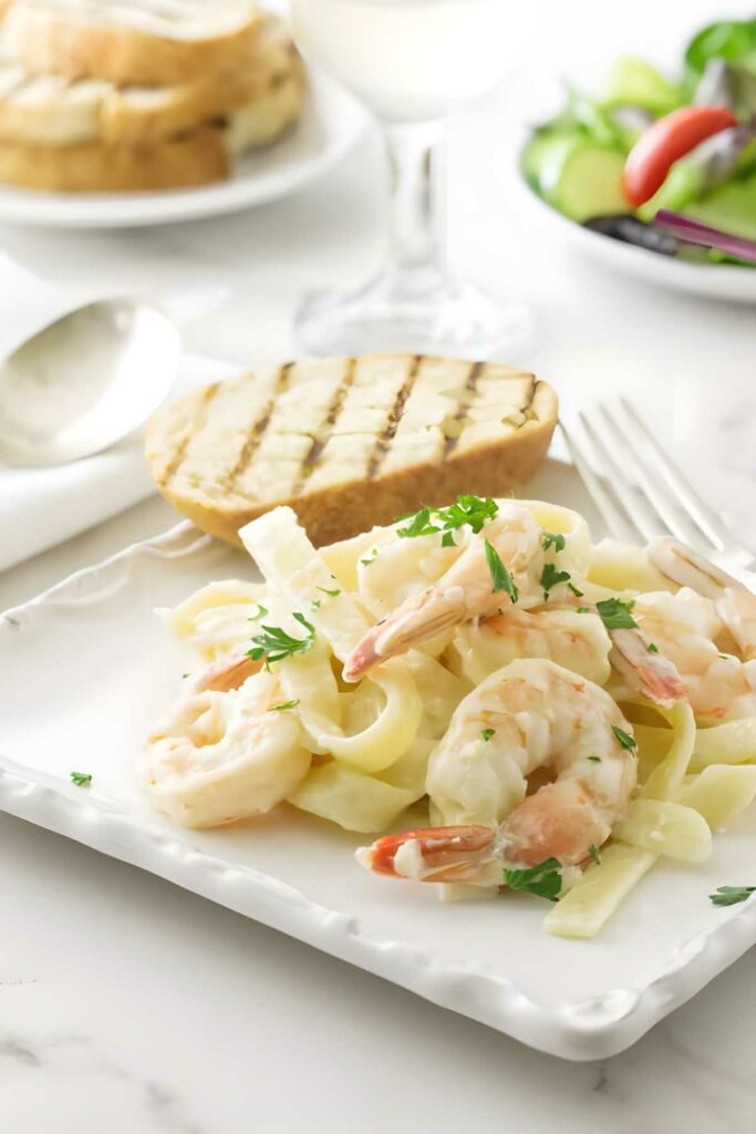 Shrimp fettuccine alfredo with parsley and grilled bread on a white table.