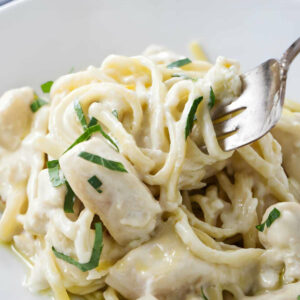 A fork swirling a bite of creamy chicken pasta with garlic butter sauce.