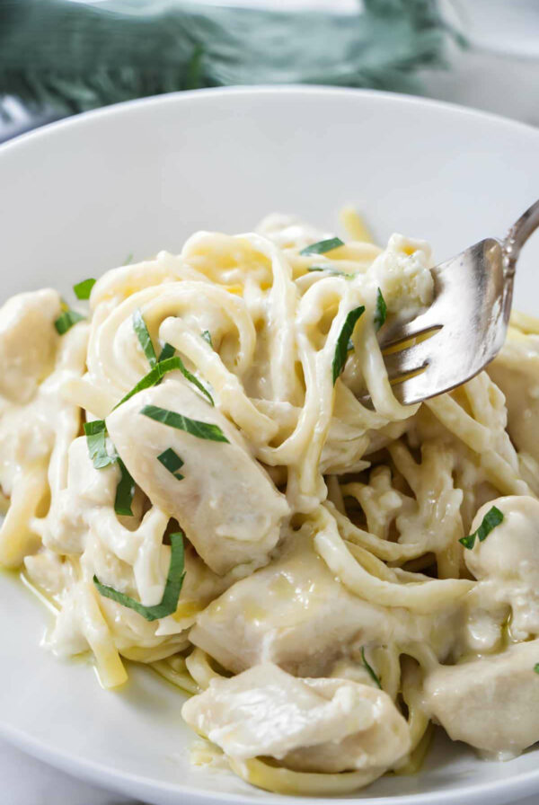 A fork swirling a bite of creamy chicken pasta with garlic butter sauce.