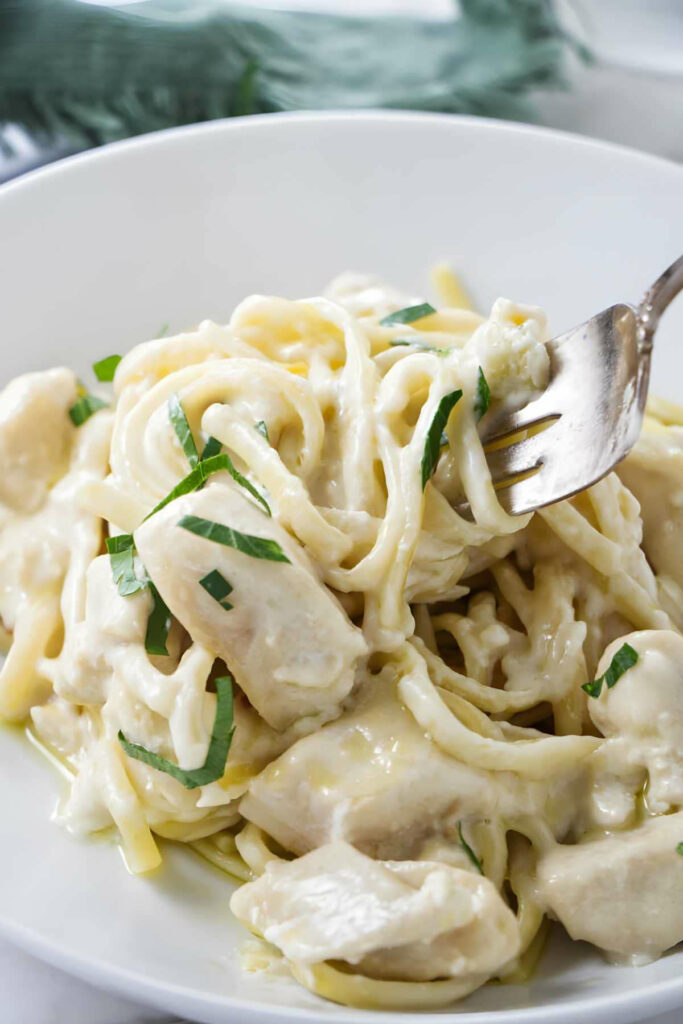 A fork swirling a bite of creamy chicken pasta with garlic butter sauce.