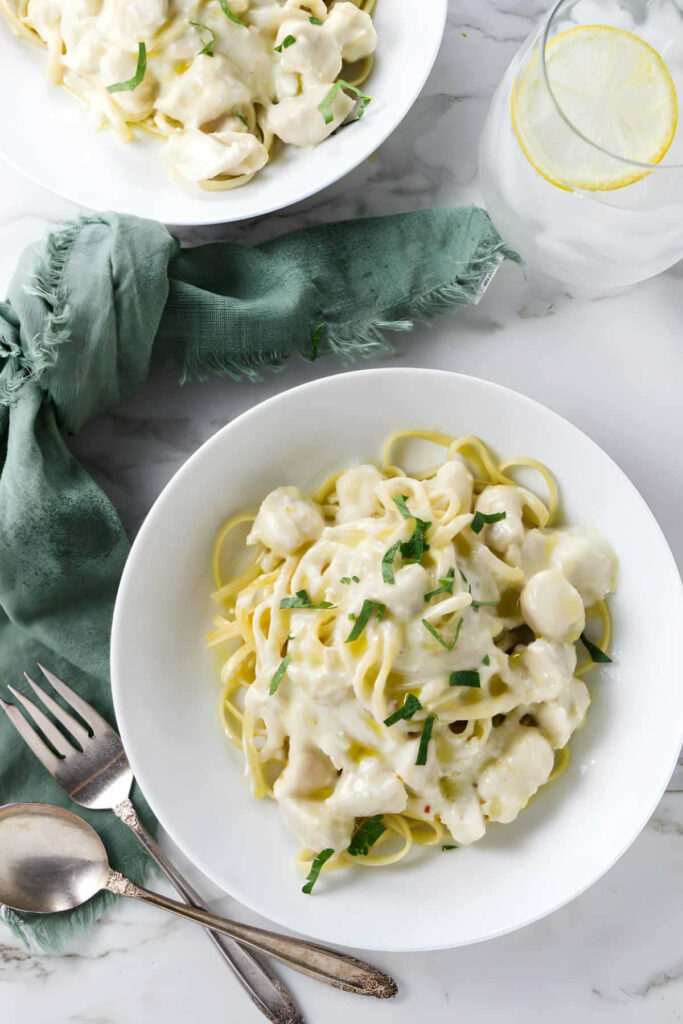 A dish of creamy garlic pasta with chicken next to a glass of water.