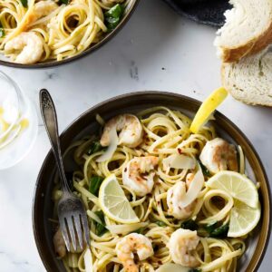 Shrimp pasta with lemon, basil, and bread on a marble table.