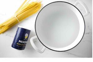 Uncooked spaghetti, Morton salt, and a white pot with water on marble.