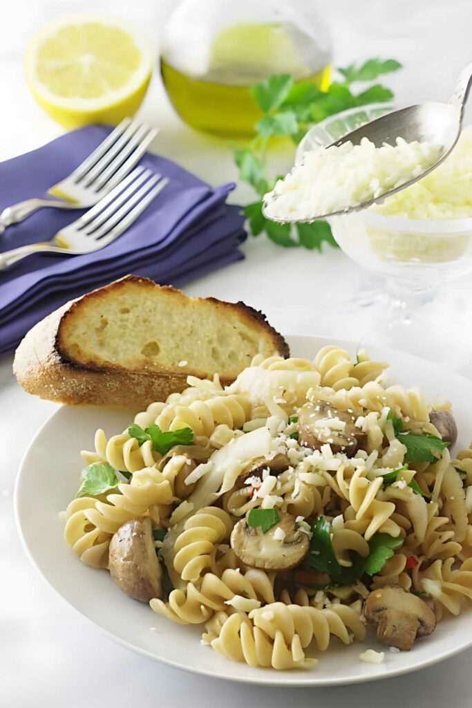 Rotini pasta with mushrooms, parsley, cheese, and toasted bread on the side.