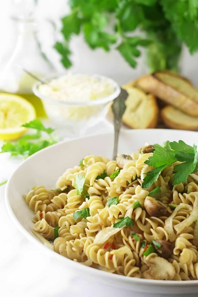 Rotini pasta with mushrooms and parsley in a white bowl on white surface.