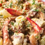Creamy lobster pasta topped with breadcrumbs and parsley, lemon slices behind.
