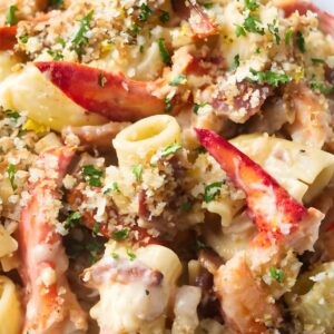 Creamy lobster pasta topped with breadcrumbs and parsley, lemon slices behind.