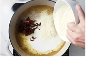 Hand pours flour into pot with melted butter and sun-dried tomatoes.