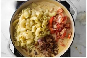 Pot of pasta with lobster, tomatoes, and creamy sauce on stovetop.