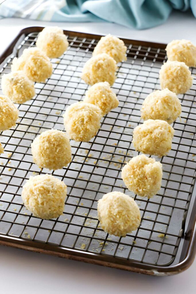 Uncooked coconut-coated dough balls on a cooling rack over baking sheet.