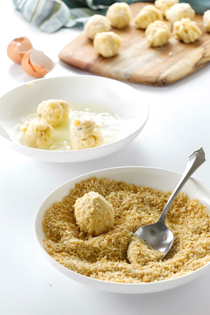 Cold mac and cheese balls coated in breadcrumbs in bowl.