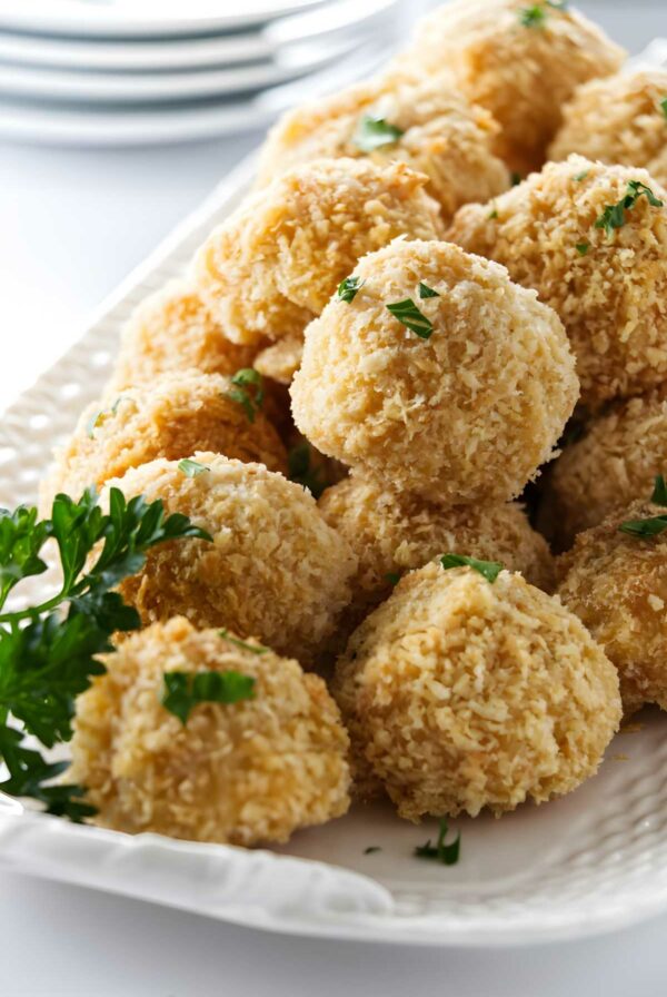 Golden, breaded mac and cheese bites with parsley on a white platter.