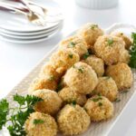 Golden baked balls with parsley on a white platter, dipping sauce behind.