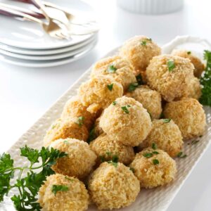 Golden baked balls with parsley on a white platter, dipping sauce behind.