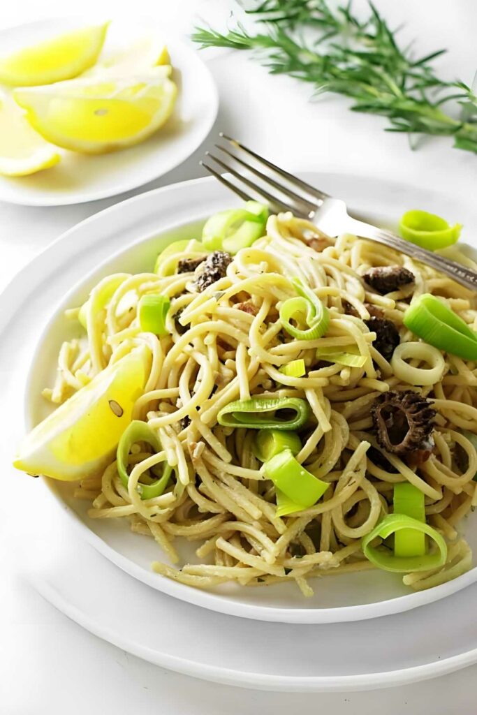 Pasta with mushrooms, lemon wedge, and a fork on the plate.