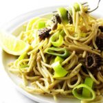 Pasta with mushrooms, lemon wedge; fork lifting pasta.
