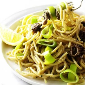 Pasta with mushrooms, lemon wedge; fork lifting pasta.