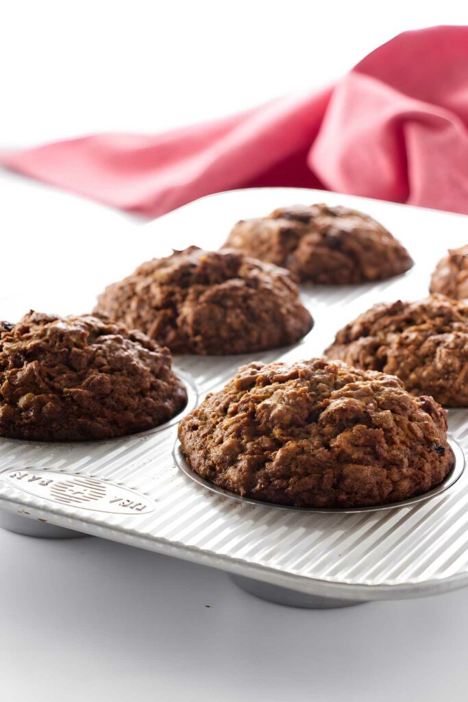 Six carrot apple muffins in a muffin tin. 