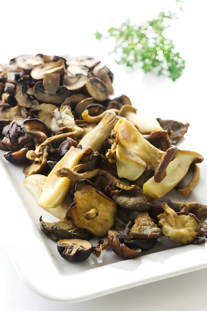 Assorted cooked wild mushrooms on a white rectangular plate.