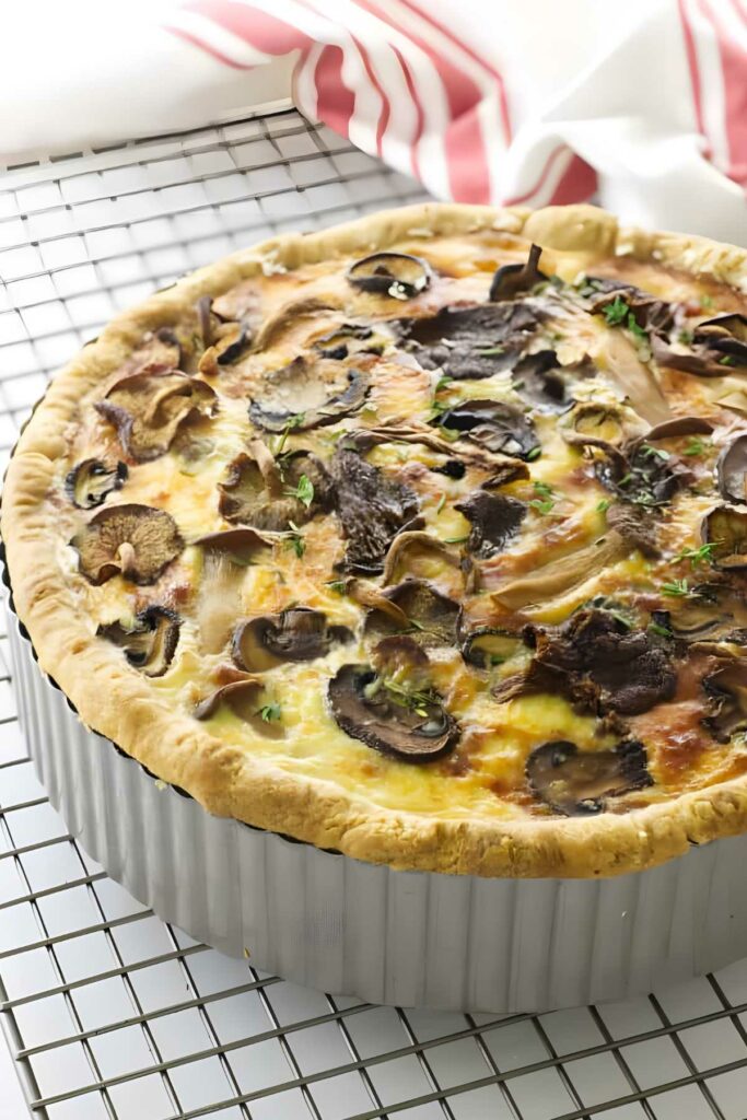 Golden mushroom quiche on cooling rack, topped with herbs and sliced mushrooms.