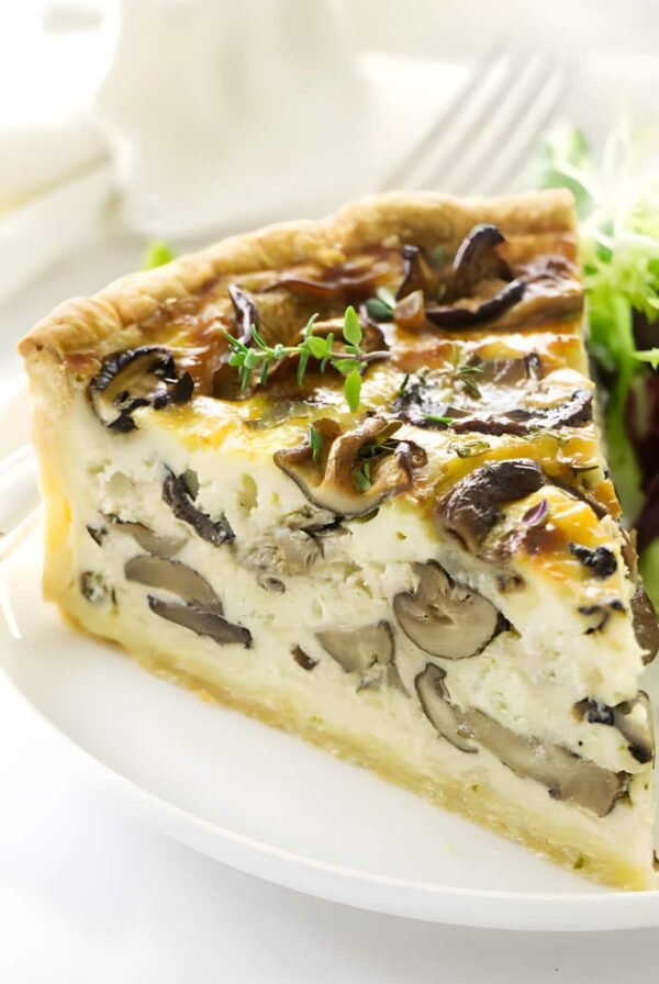Mushroom quiche slice with herbs on white plate, side of greens.