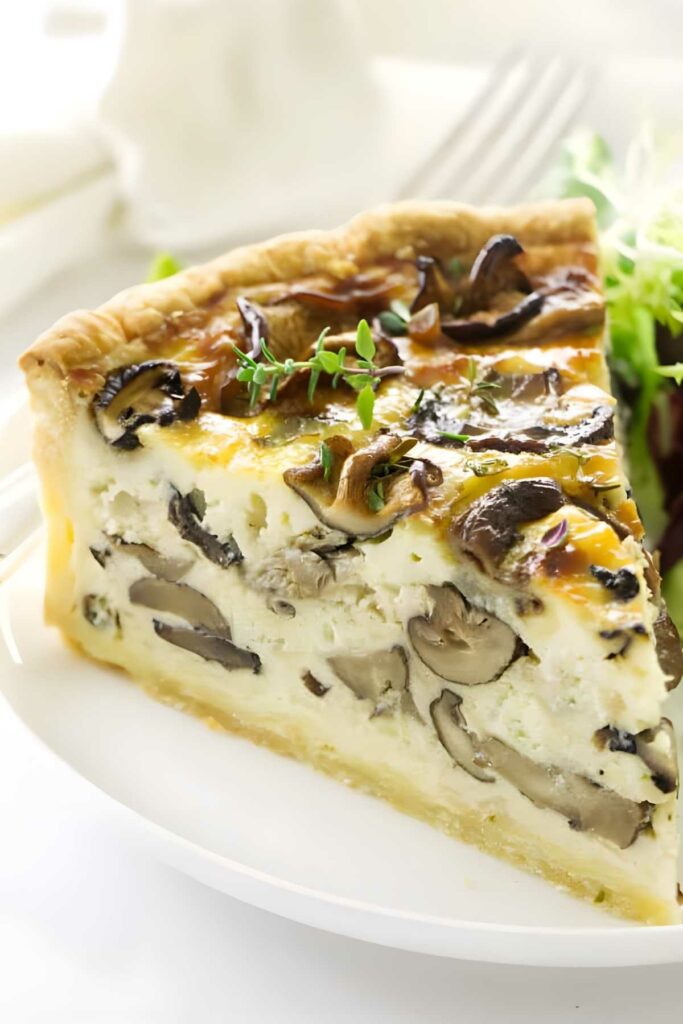 Mushroom quiche slice with herbs on white plate, side of greens.