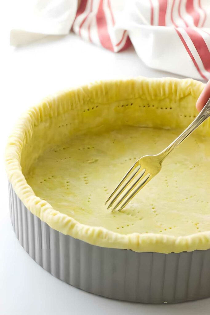 Hand poking fork holes in unbaked pie crust in metal pan.