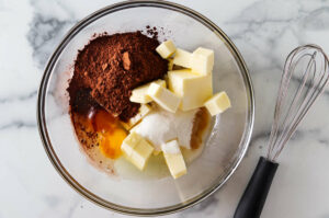 Combining butter with sugar, eggs, and cocoa powder.