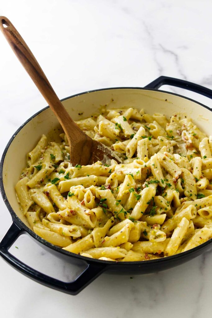 Pistachio sauce pasta in a skillet with a wooden spoon.