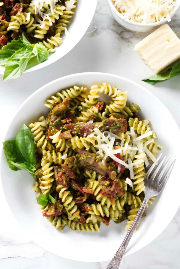 Bowl of green pesto pasta with cheese, basil, and prosciutto.