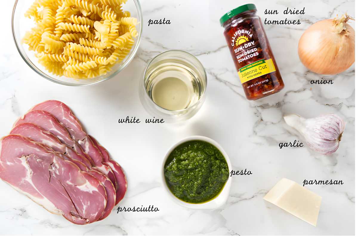 Pasta dish ingredients arranged on marble: pasta, prosciutto, pesto, wine, sundried tomatoes.