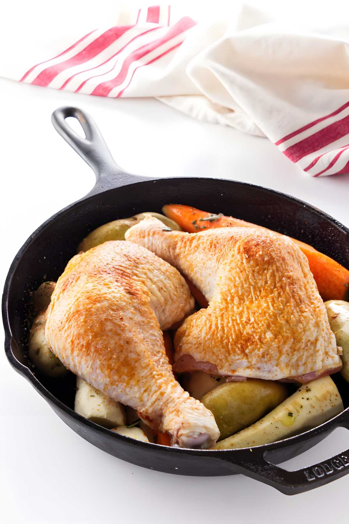 Roasted chicken leg quarters on potatoes and carrots in a cast iron skillet.