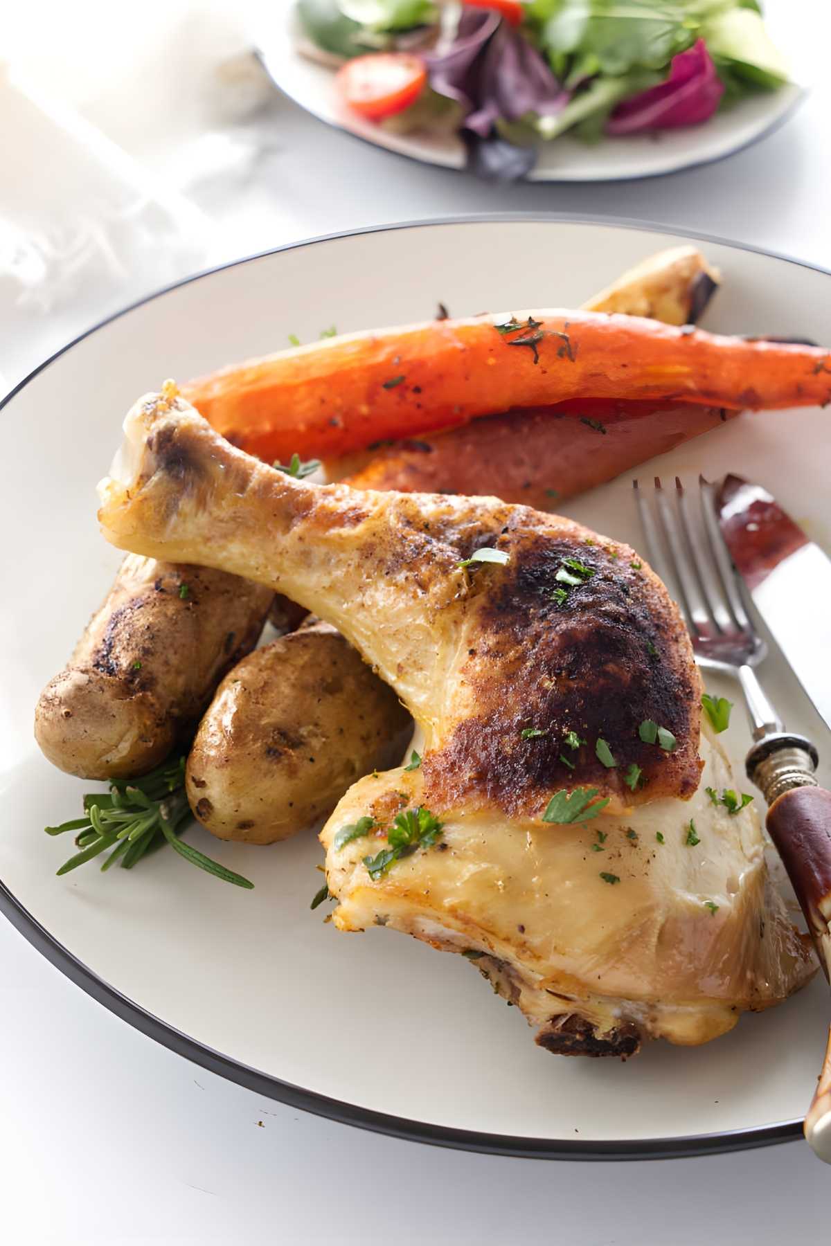 Roasted chicken quarters with potatoes and carrot on a plate, salad in background.