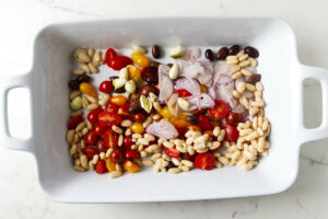 Adding tomatoes, shallots, white beans, and garlic to a baking dish.