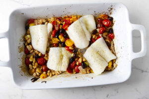 Nestling cod into the baking dish with tomatoes, beans, garlic, and olives.